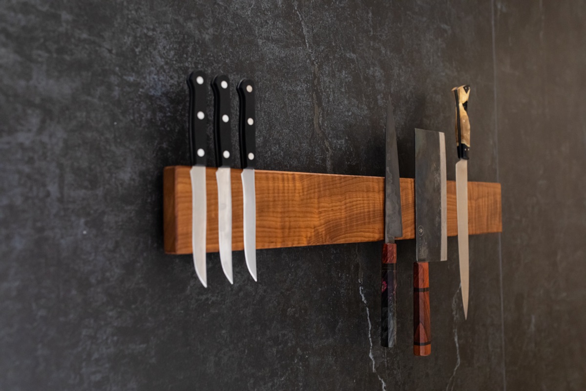 A wooden BAR XL holding kitchen knives against a dark wall